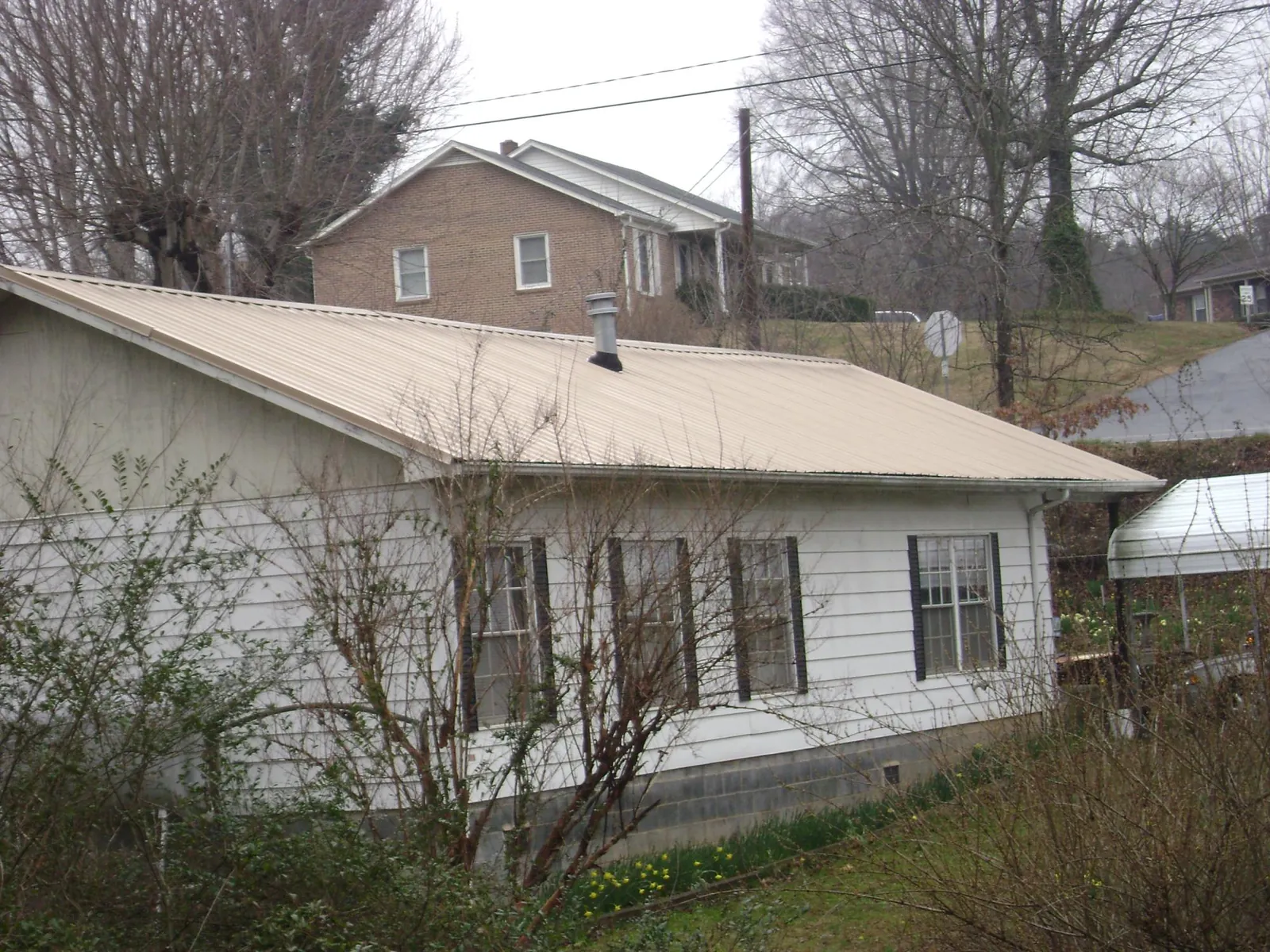 Tan metal roof on a white sided house set into a hillside — Commercial Roofing by Roofing Brothers in Ephrata